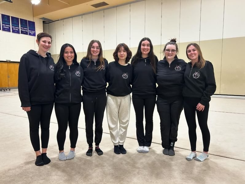 The Rhythmic Gemstones coaching team standing together in a school gym.