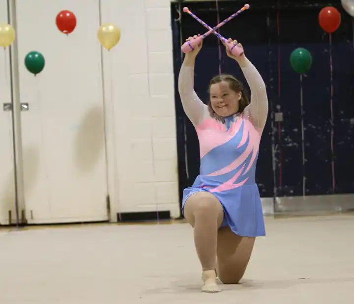 A Special Olympics athlete kneeling with clubs raised overhead.