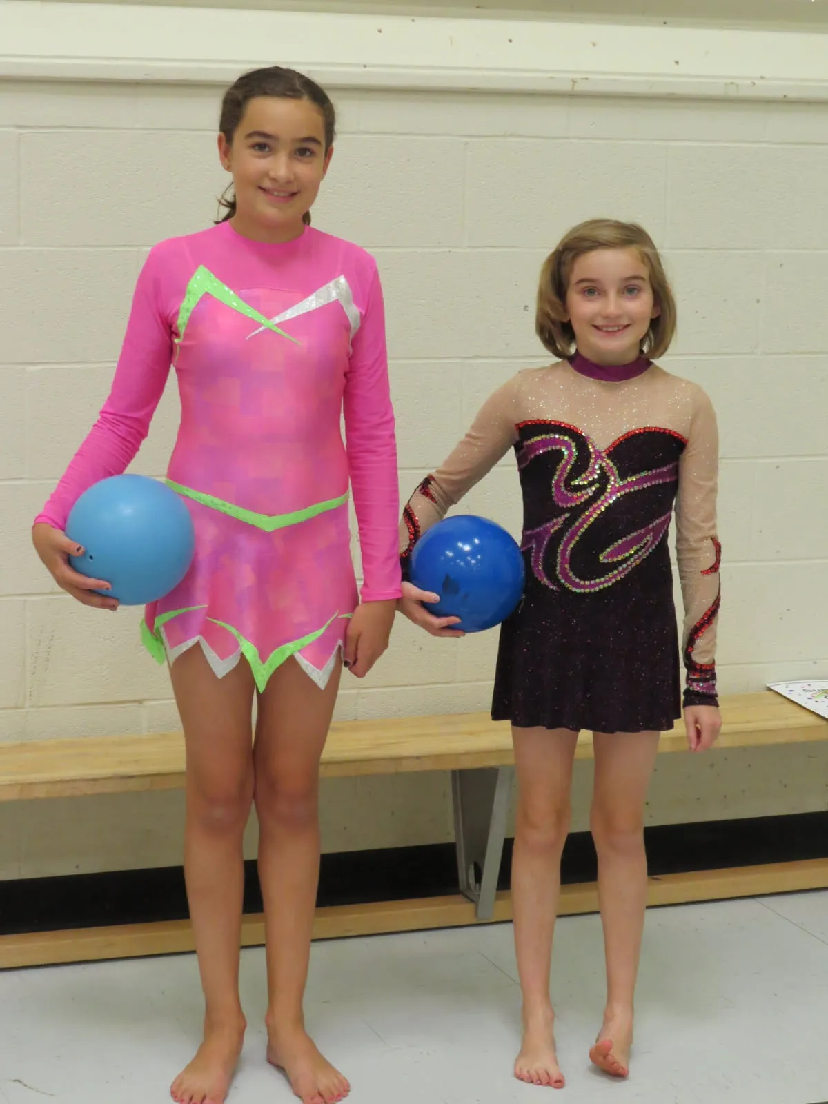 Two gymnasts in competition leotards smiling with their balls.