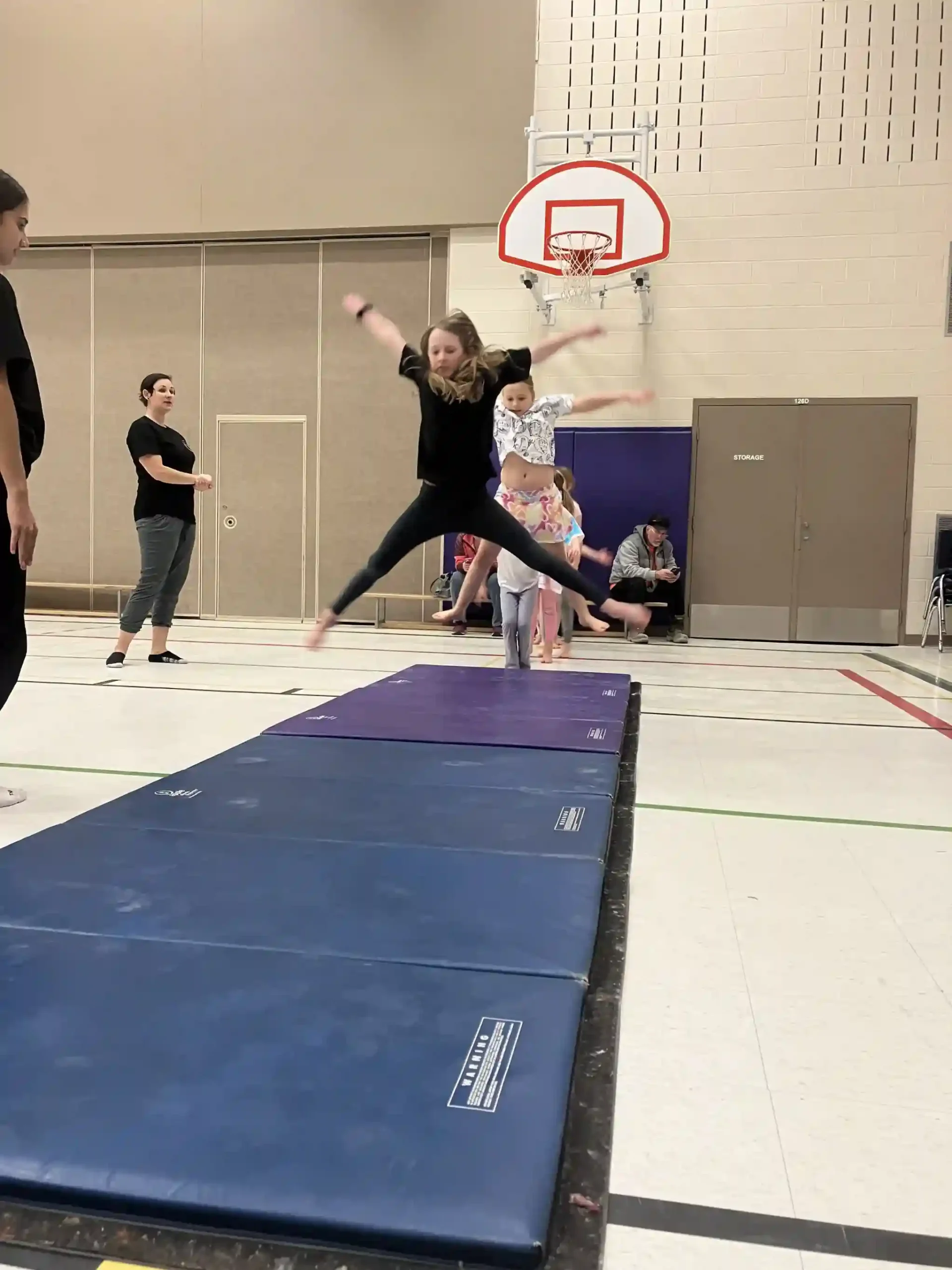 A gymnast leaping across a blue mat in a school gym.
