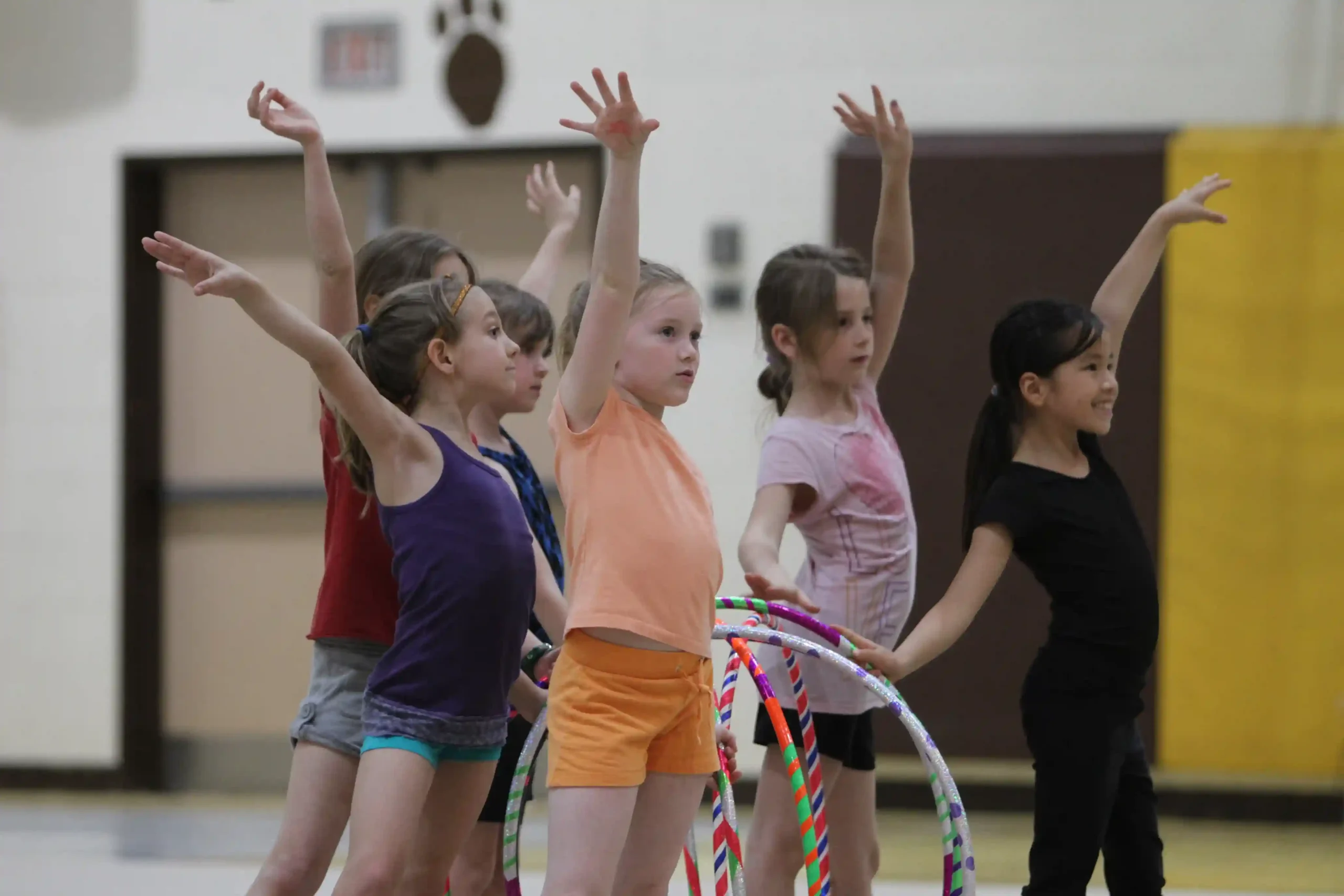 Young gymnasts with arms raised, holding hoops at the end of a routine.